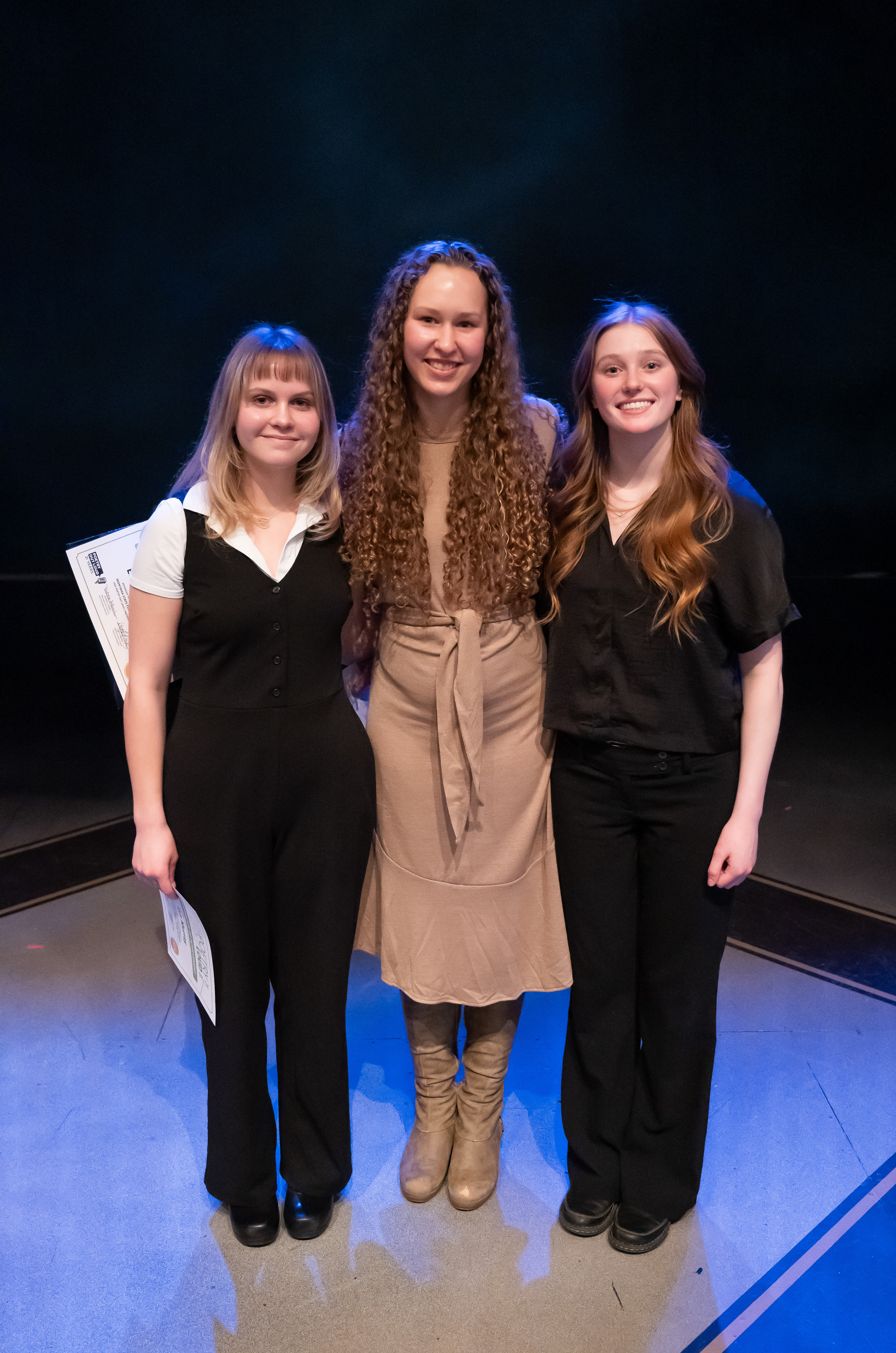 Eva Murray, in black vest and slacks, Ellette Whitcomb, in beige dress, and Samantha Symington, in black shirt and pants, pose together on stage.